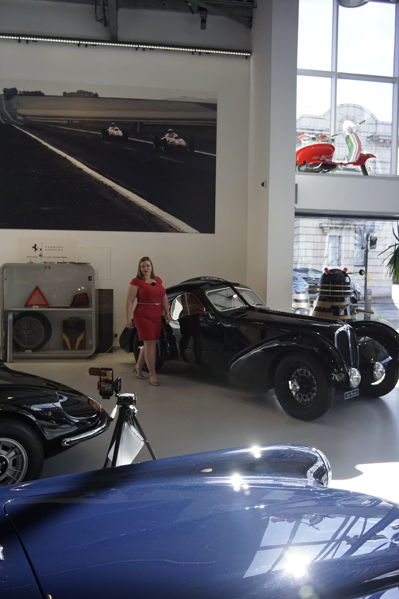 Vivian De Vere beside a vintage car in a showroom